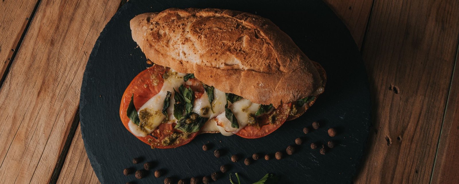 A freshly made ciabatta sandwich with cheese, tomato, and herbs on a rustic wooden table.